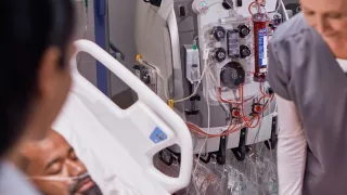 Two healthcare professionals at the patient bedside in front of the PrisMax system