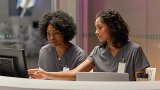 Two nurses review data on a desktop device in the ICU