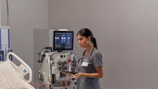 Healthcare professional at the patient bedside in front of the PrisMax System