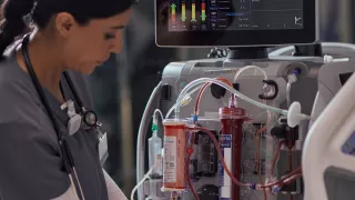 Healthcare professional at the patient bedside in front of the PrisMax System with an Oxiris set attached to it
