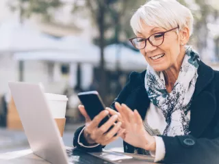 A woman uses a mobile device and laptop while sitting down outside