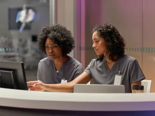 Two nurses review data on a desktop device in the ICU