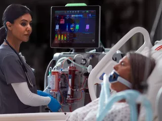 A clinician uses the PrisMax system at a patient's bedside