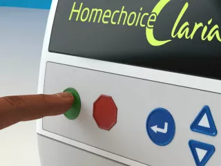 A finger touches a green button on the Homechoice Claria APD System