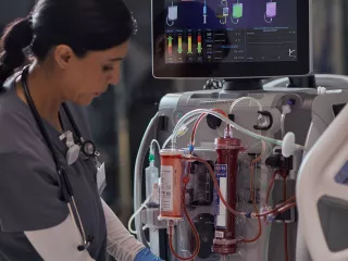 Healthcare professional at the patient bedside in front of the PrisMax System with an Oxiris set attached to it